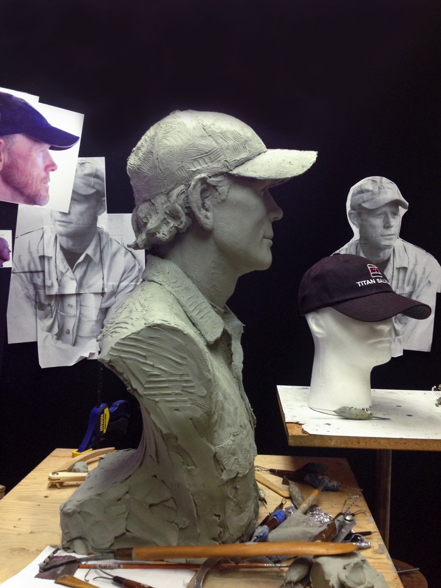 Clay portrait sculpture of Ron Howard with reference photographs and cap used during the sculpting process